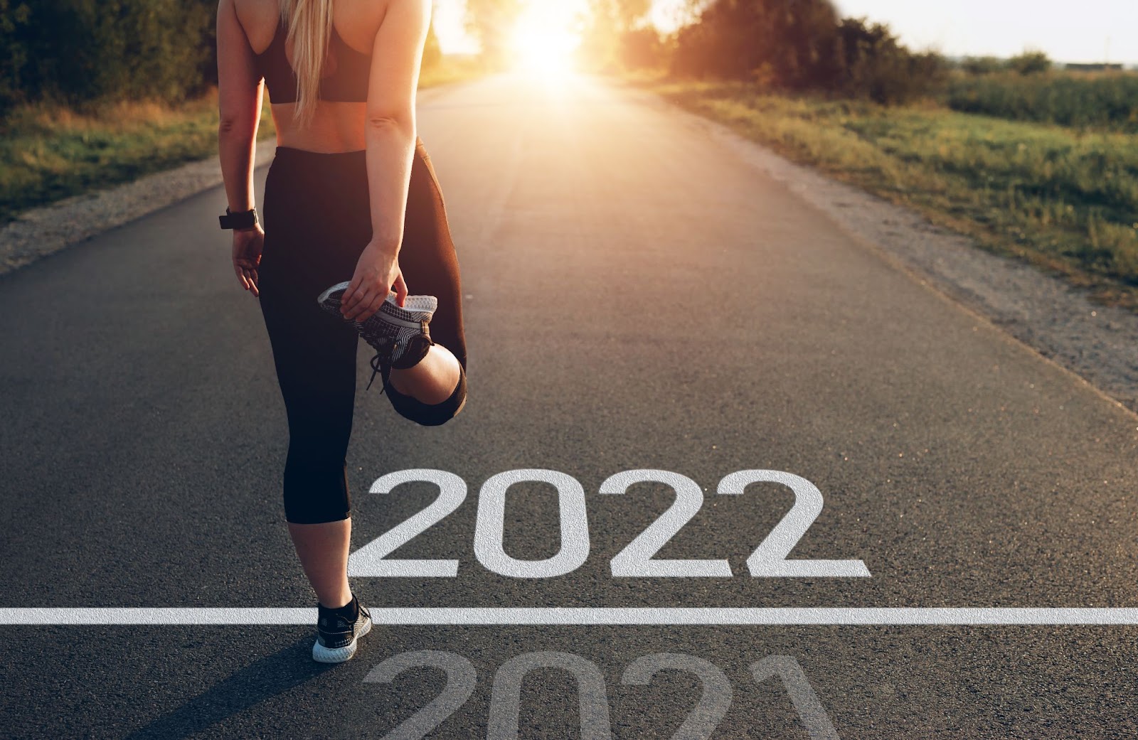 Image of young fit woman, stretching on a road, standing between a written 2021 and 2022 on the ground.