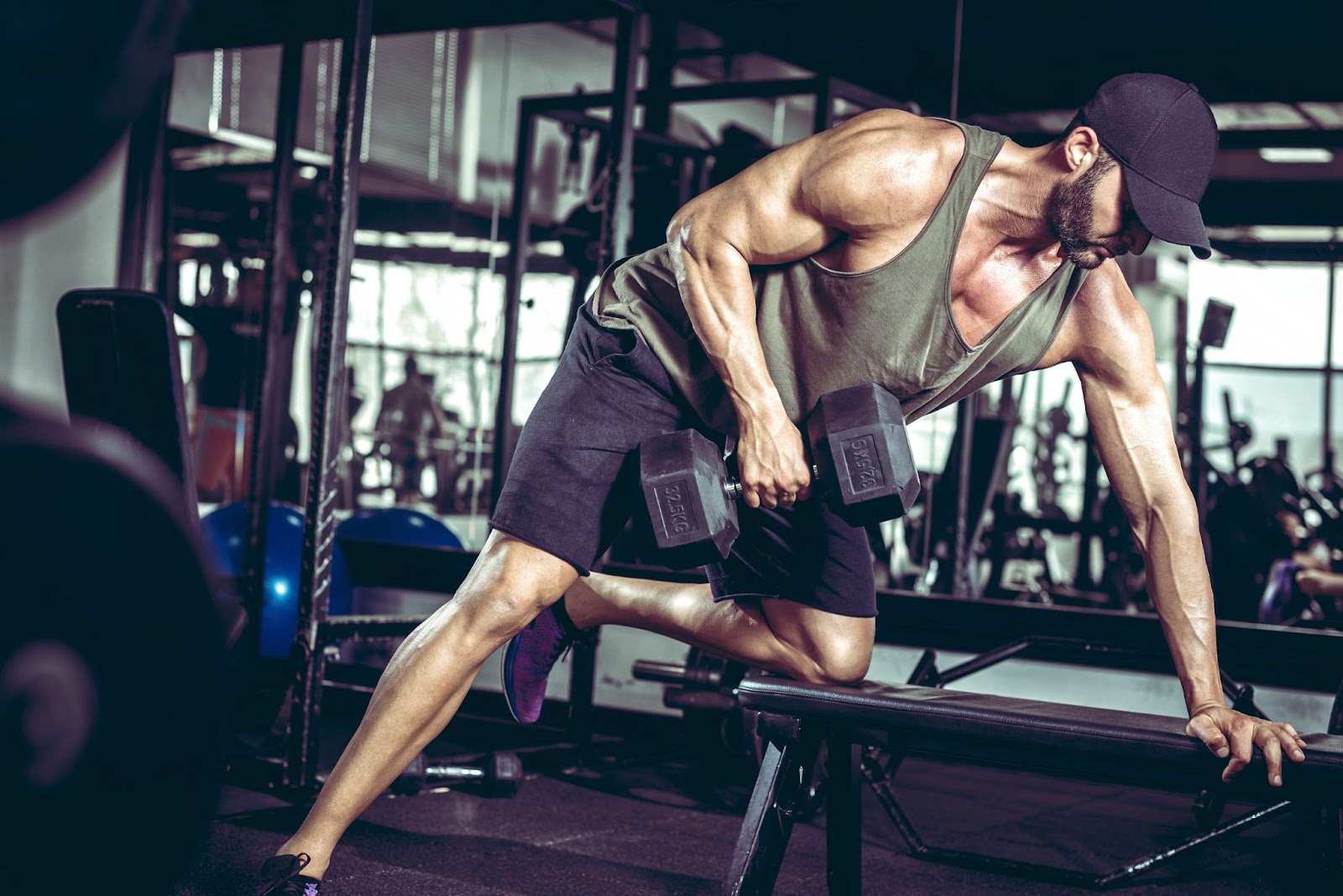 Muscular caucasian man performing a bent leg, single-arm dumbbell row pull workout.