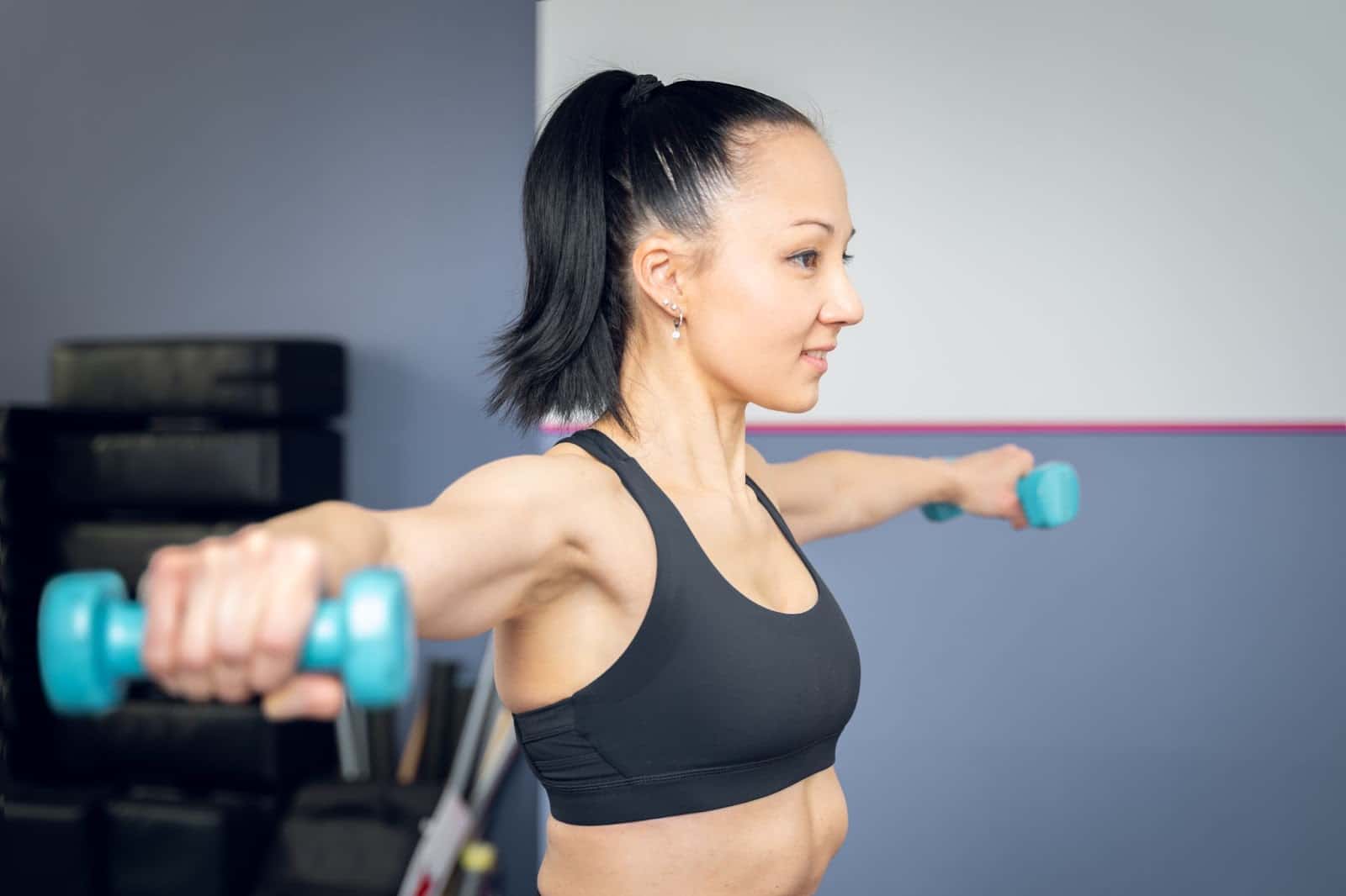 Young black-haired ethnic woman performing a lateral raise push workout with 2 pound weights.