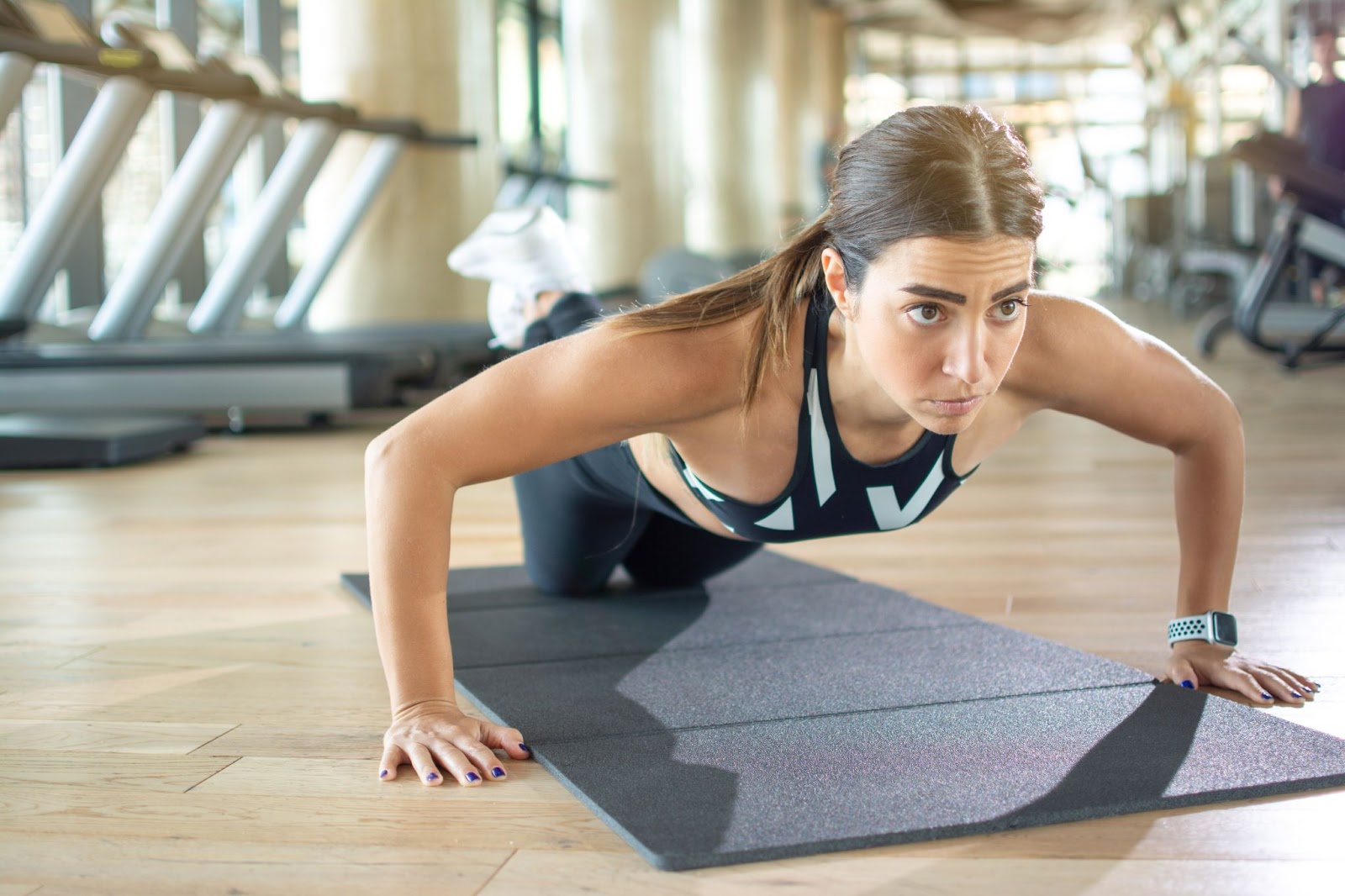 Young brunette woman performing push ups with her knees on a mat below her.