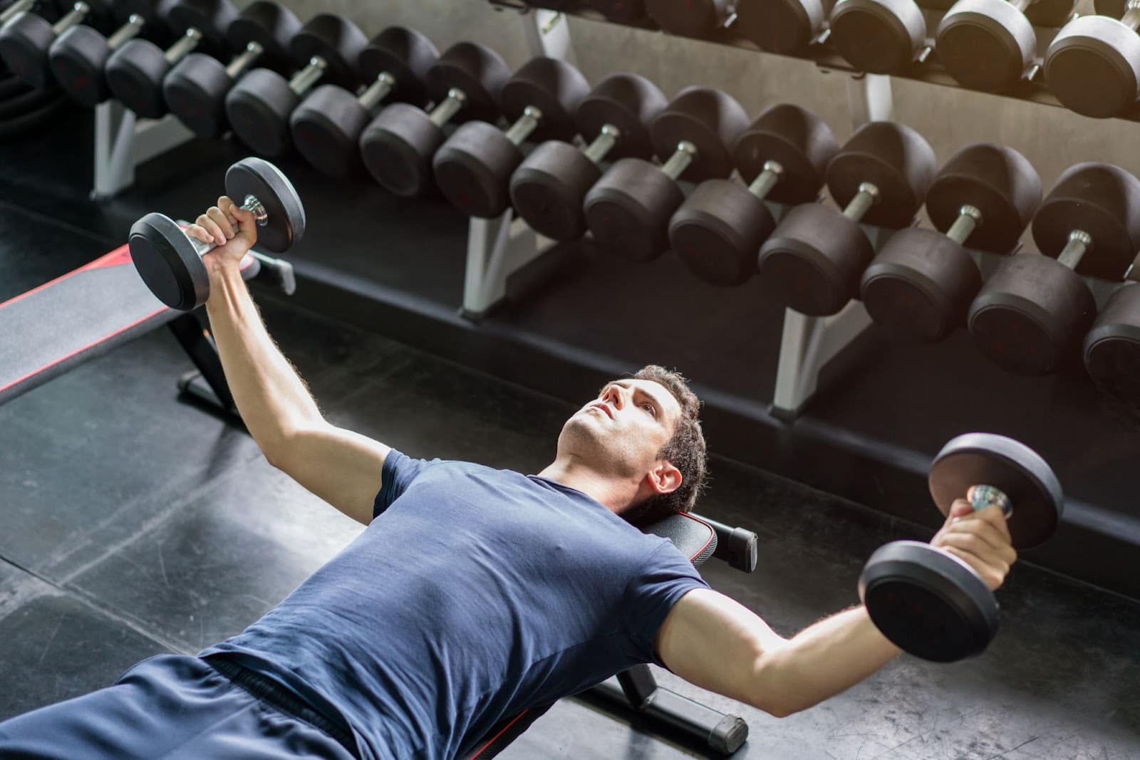 Young man performing a chest fly push workout with two dumbbells in his hands.