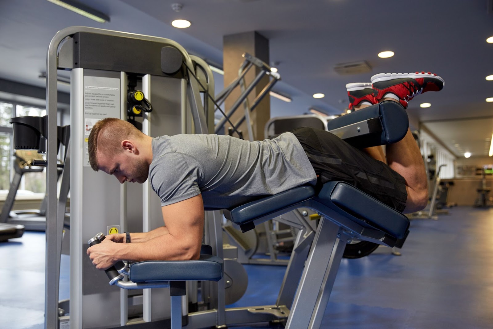 Muscular man laying on his chest, performing leg curls.