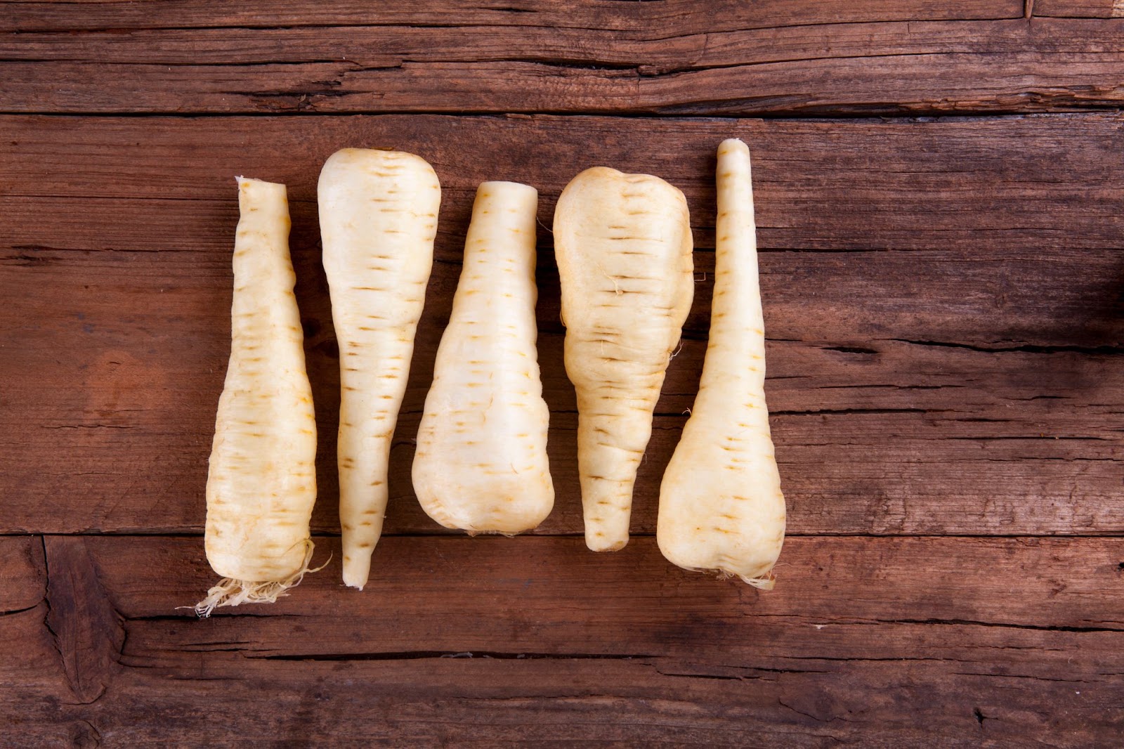 5 parsnips lined up back to back on a board.