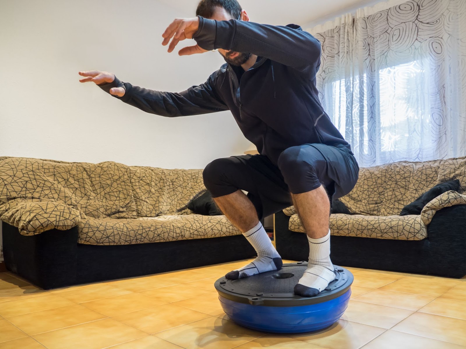 Bearded man in a deep squat on his BOSU ball in his living room.