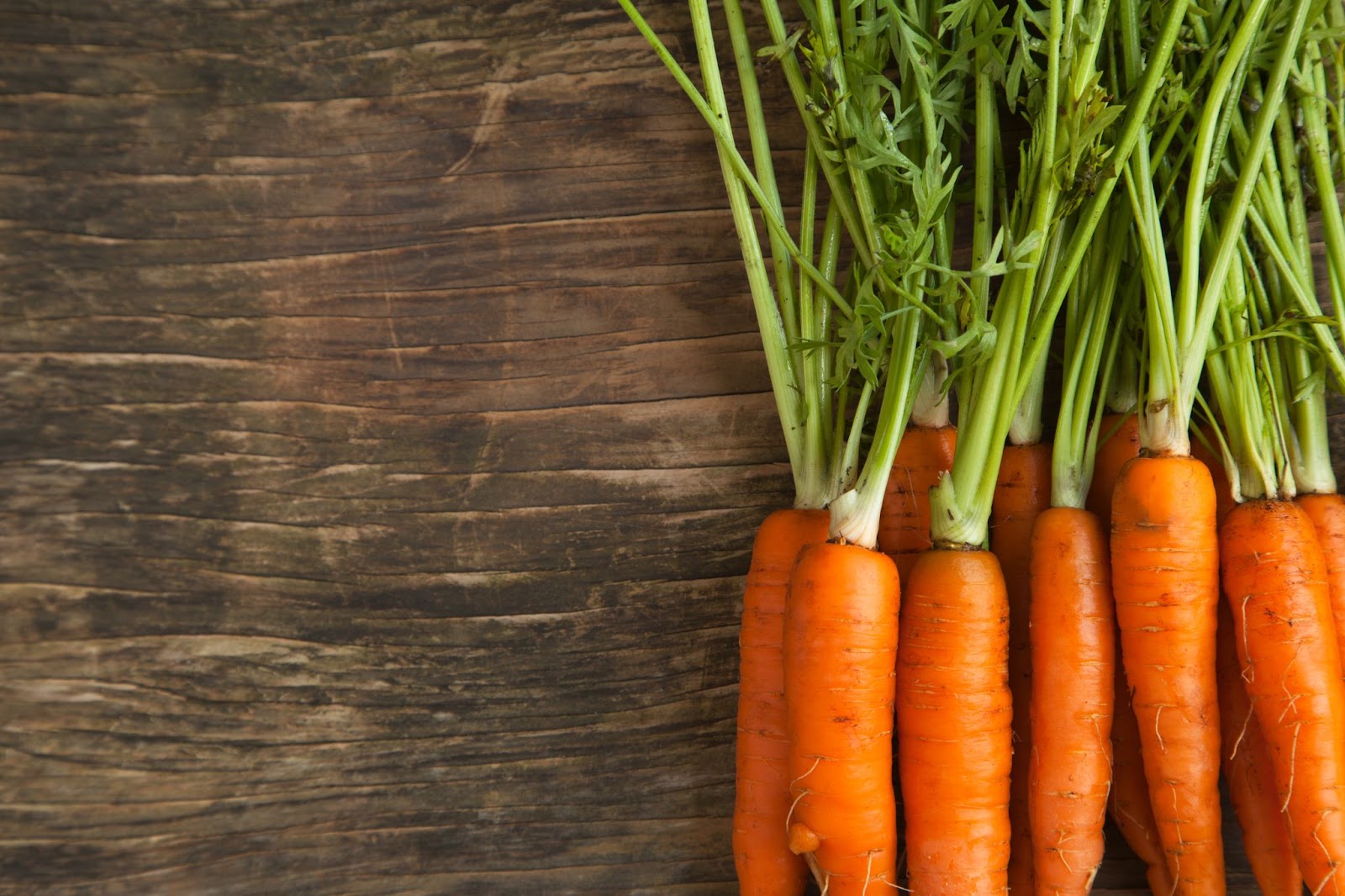 Long-stemmed carrots in a row on a wooden background. 