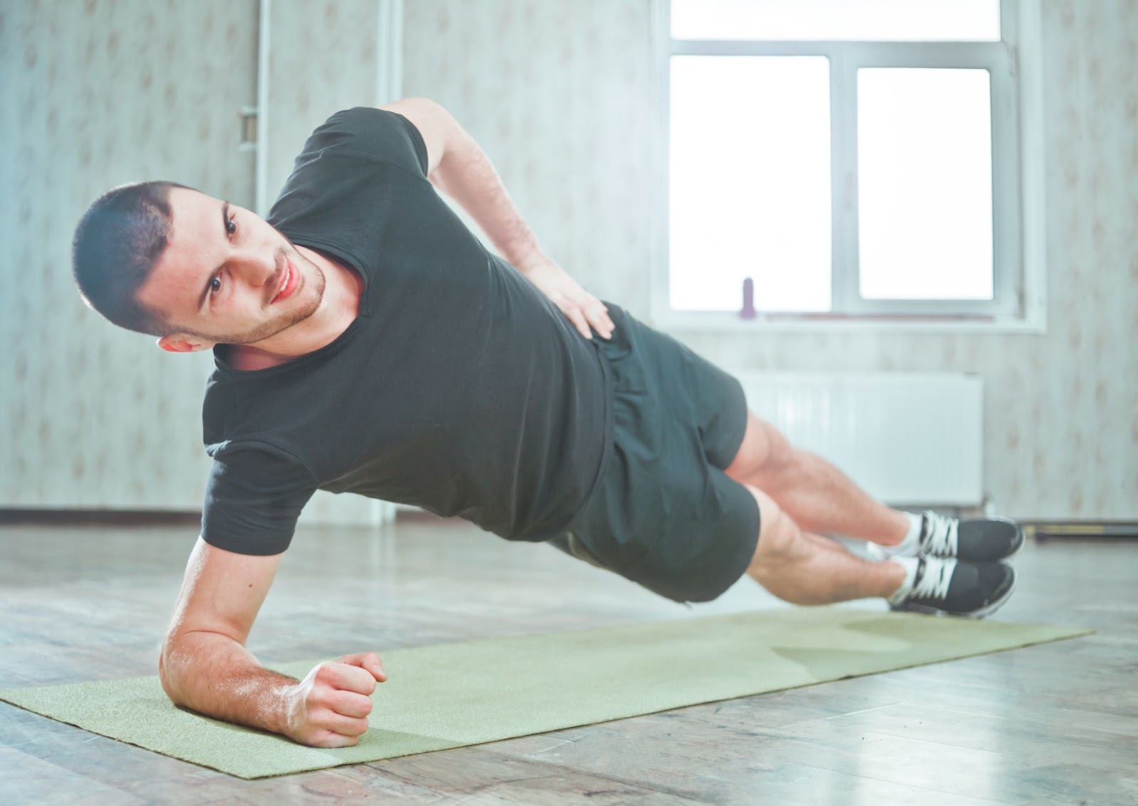 Man performing side plank on a workout mat at a gym.