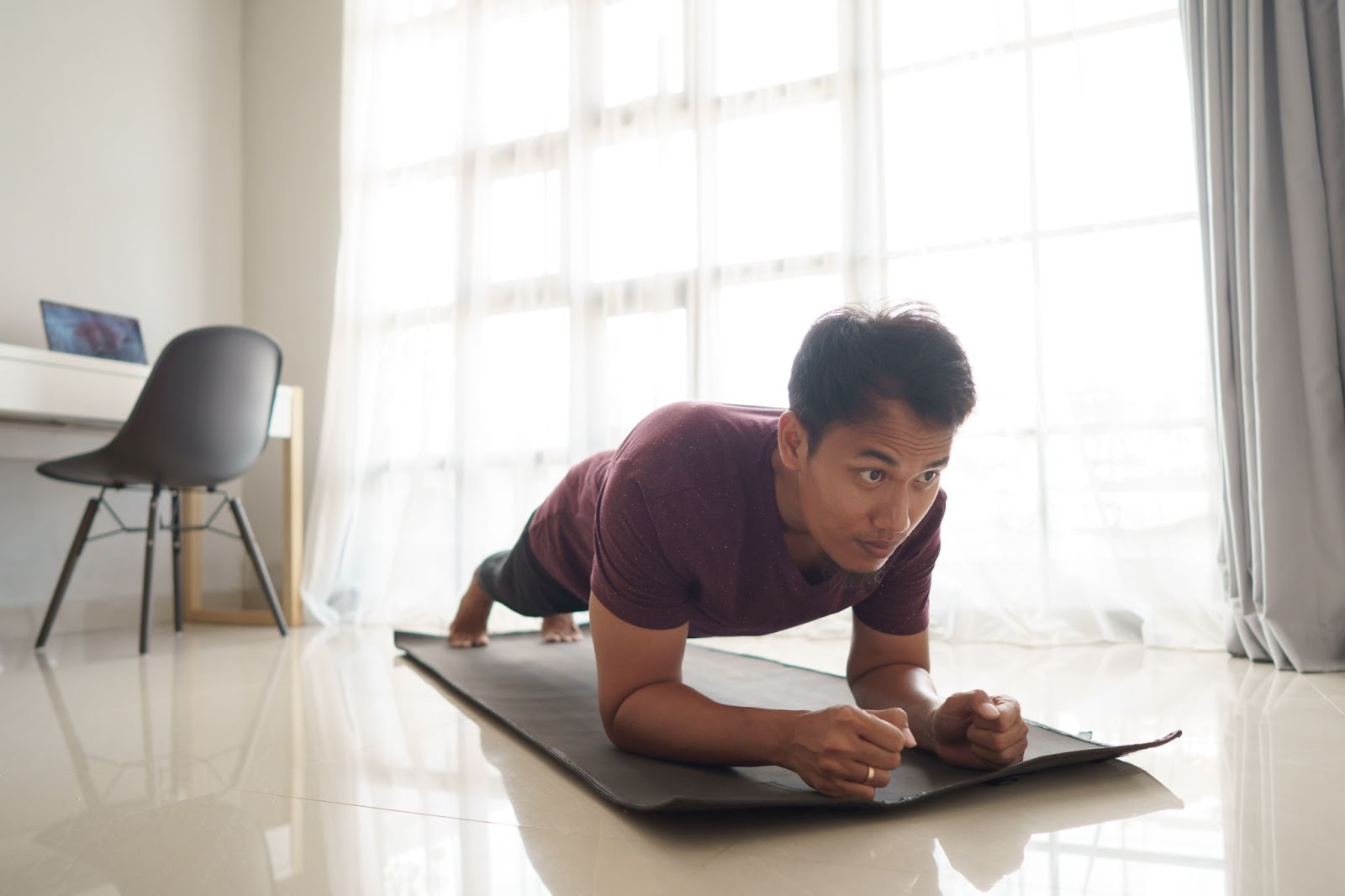 Tanned Asian man performing a plank at home.