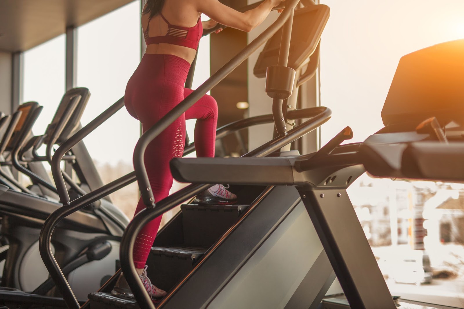 Woman in magenta workout clothes is working out on a stair stepper machine.