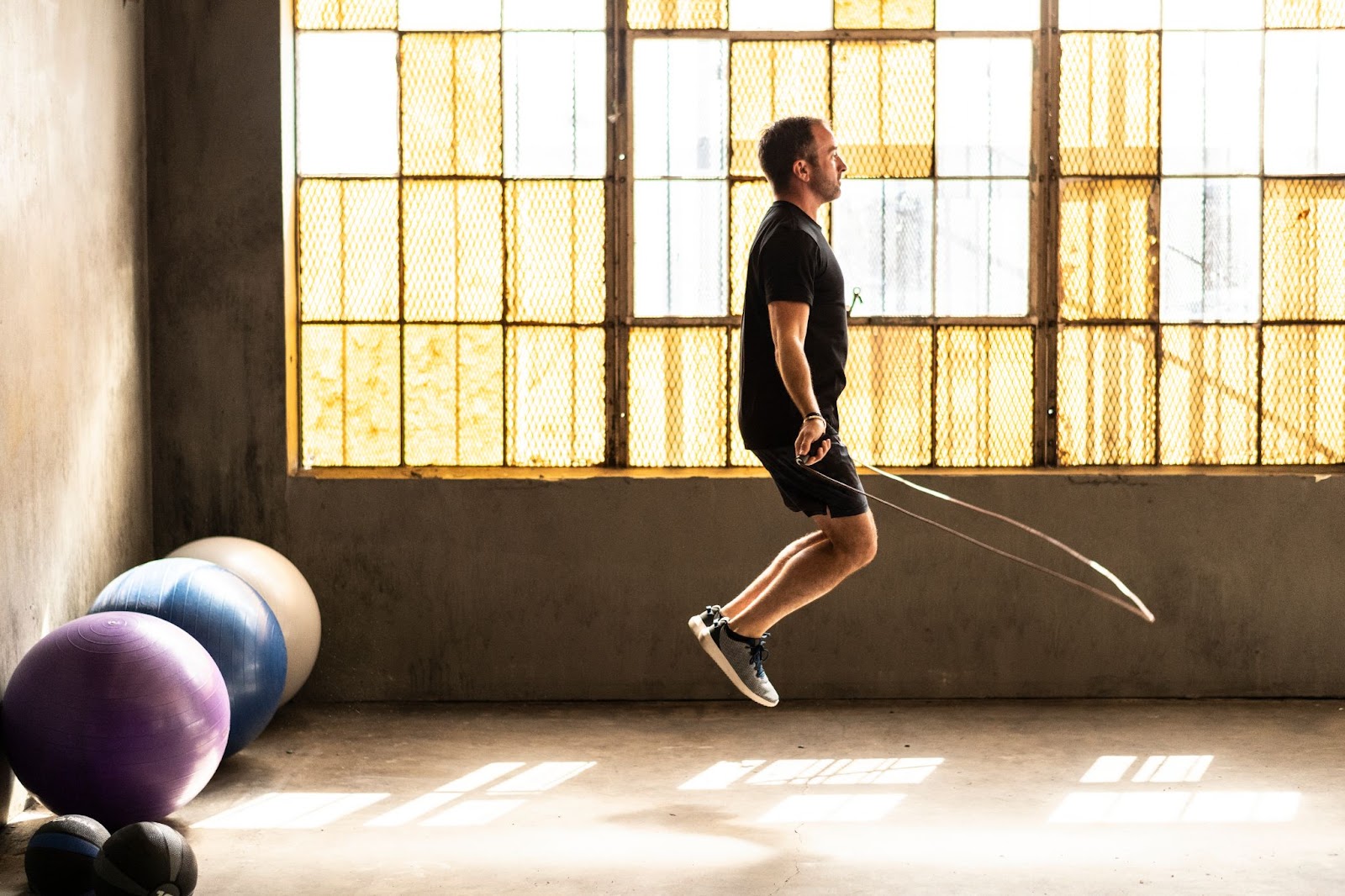Man jumping rope in an industrial fitness gym, with medicine and yoga balls behind him
