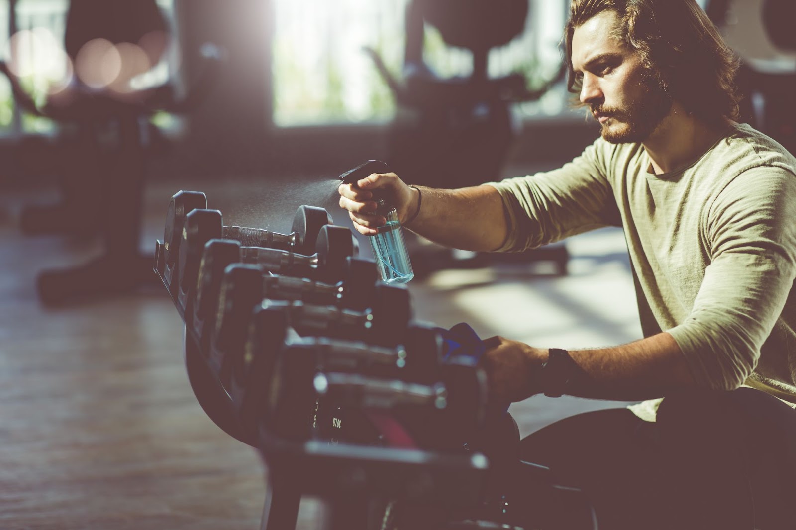 Young man spraying antibacterial solution on dumbbells in a fitness studio