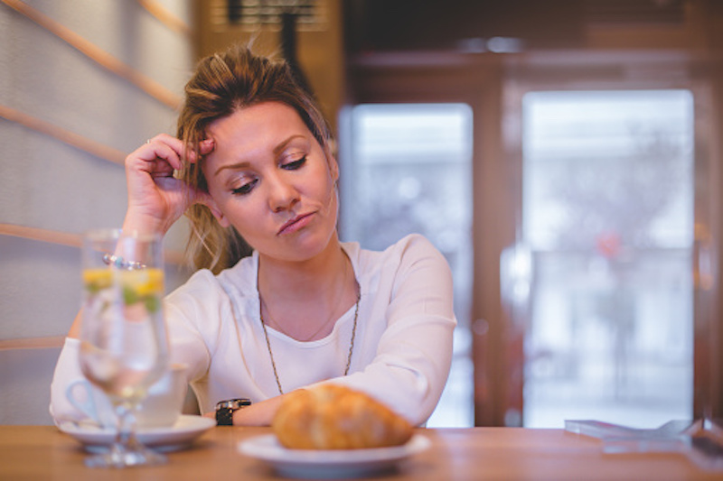 Young blonde stressed woman staring at a croissant at table