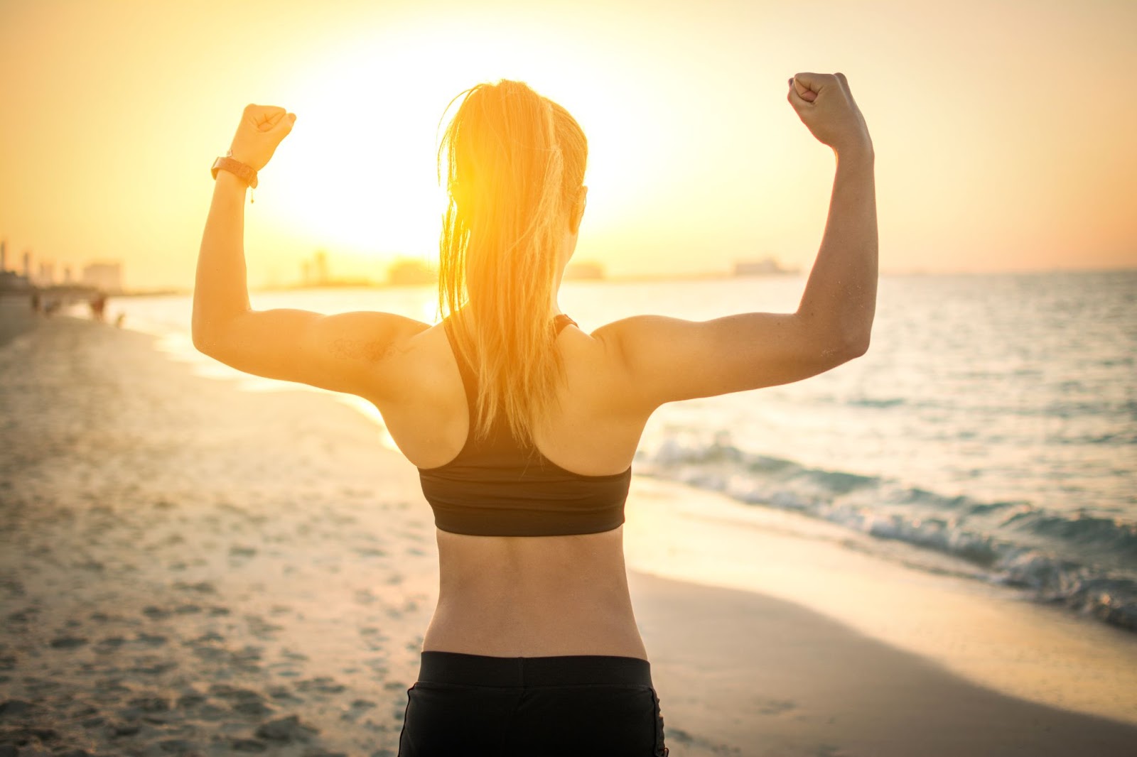 Young fit woman flexing muscles at the beach