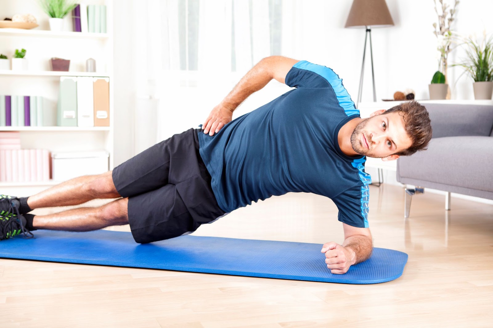 Man in blue performing a side plank at home