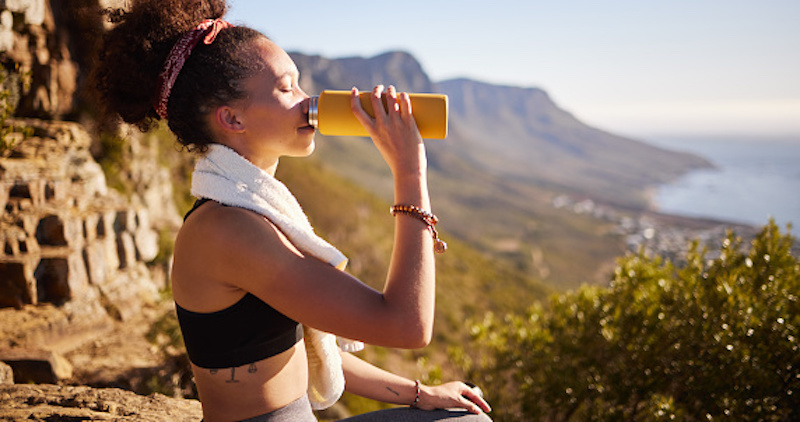 Young woman sitting on a cliff, drinking a post-workout beverage
