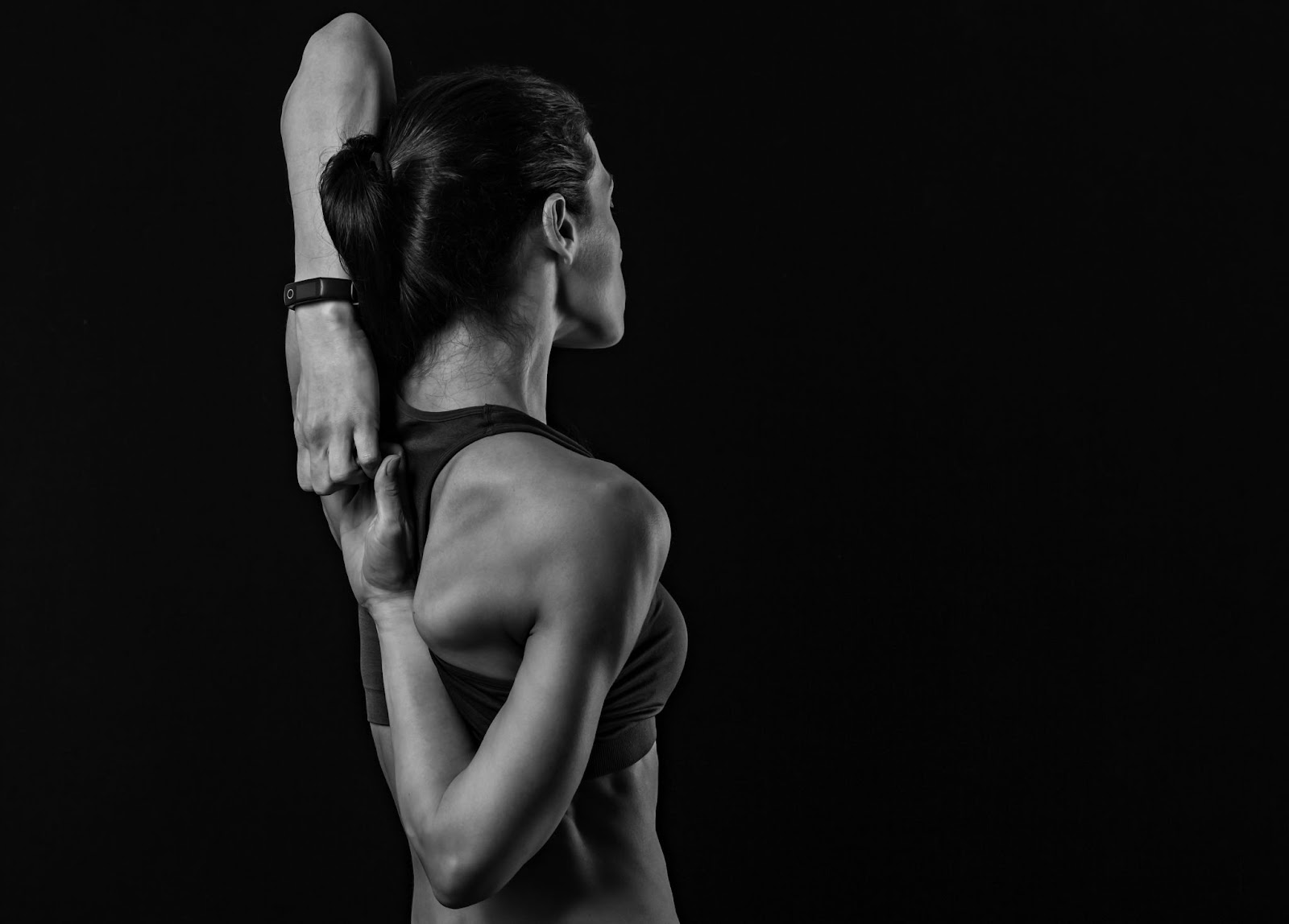 Black and white image of woman from the back, stretching her rotator cuff