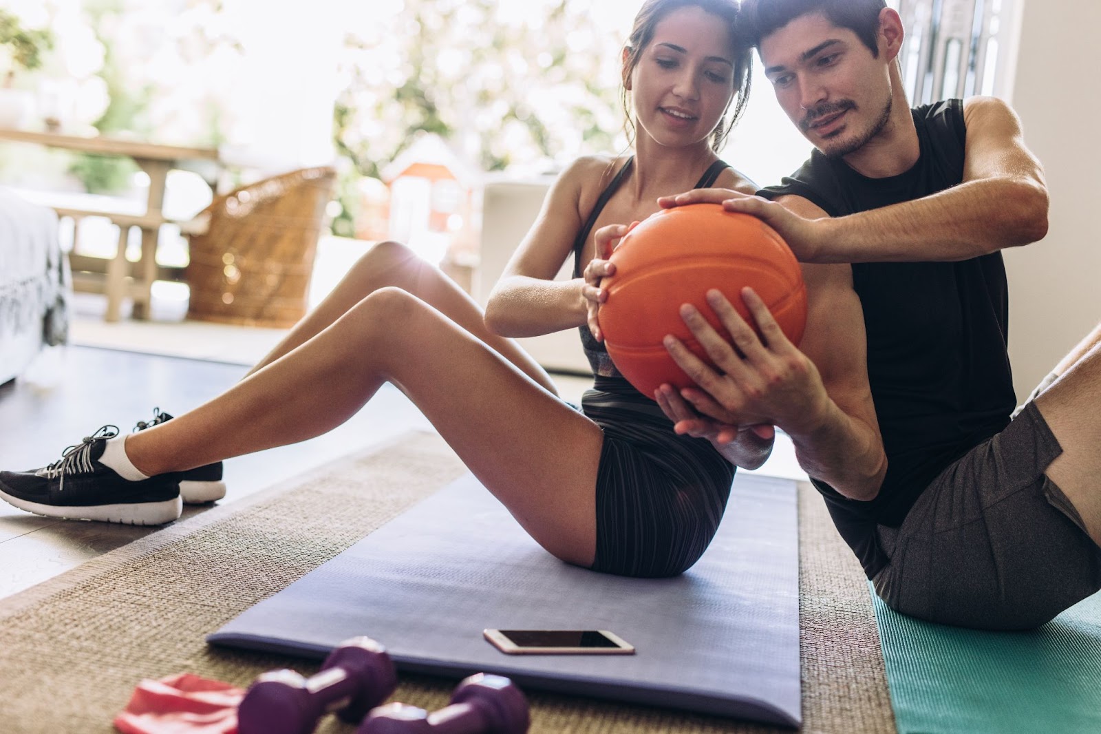 Attractive young couple passing a medicine ball while leaning on each other’s backs