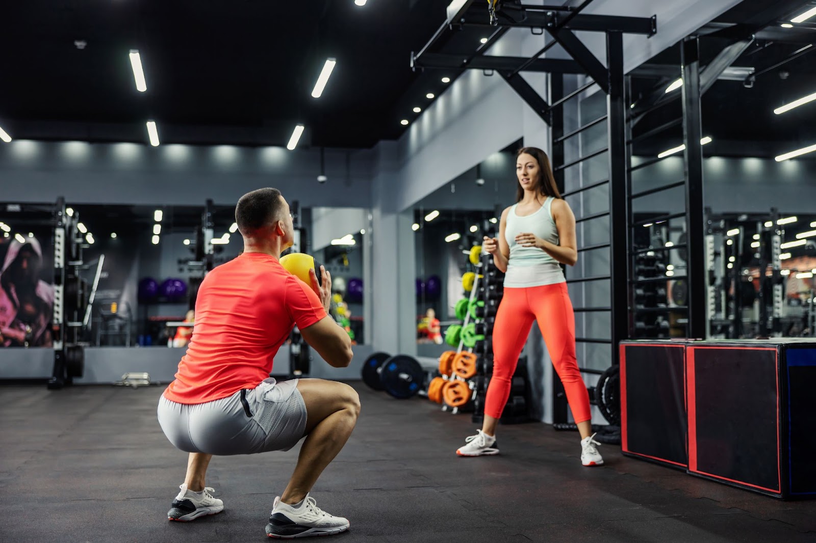 Couple performing a squat and throw in a gym, with a medicine ball