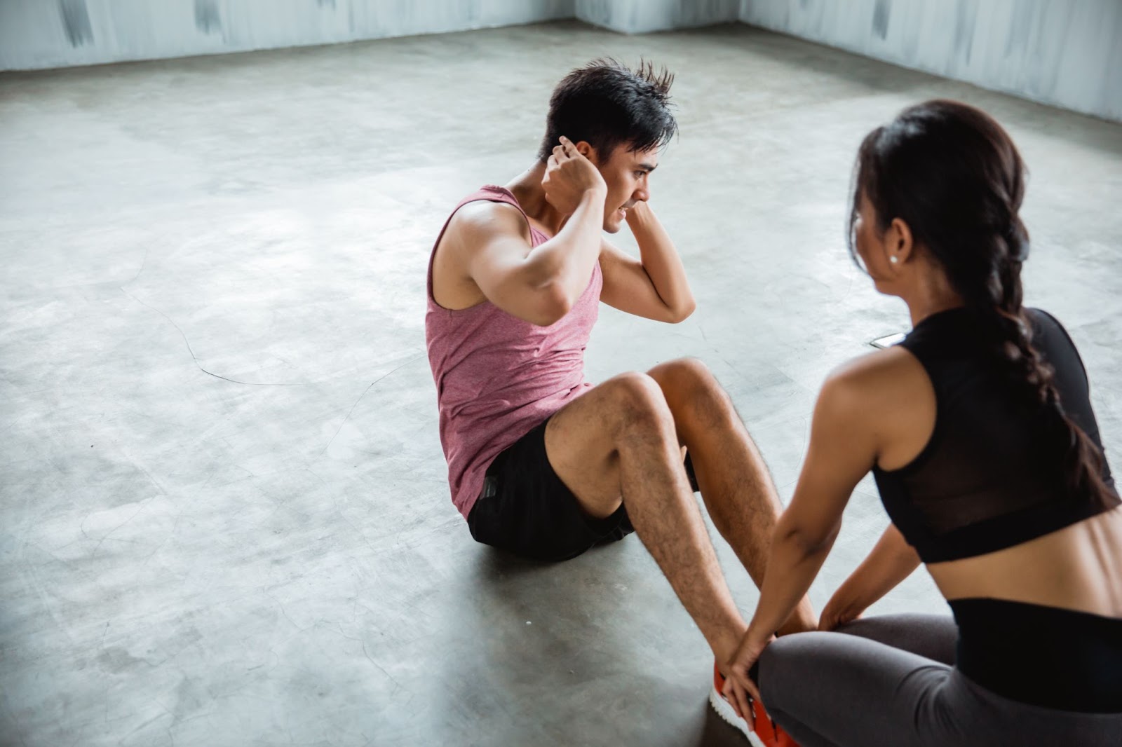 Couples doing sit ups together, woman holding man’s ankles