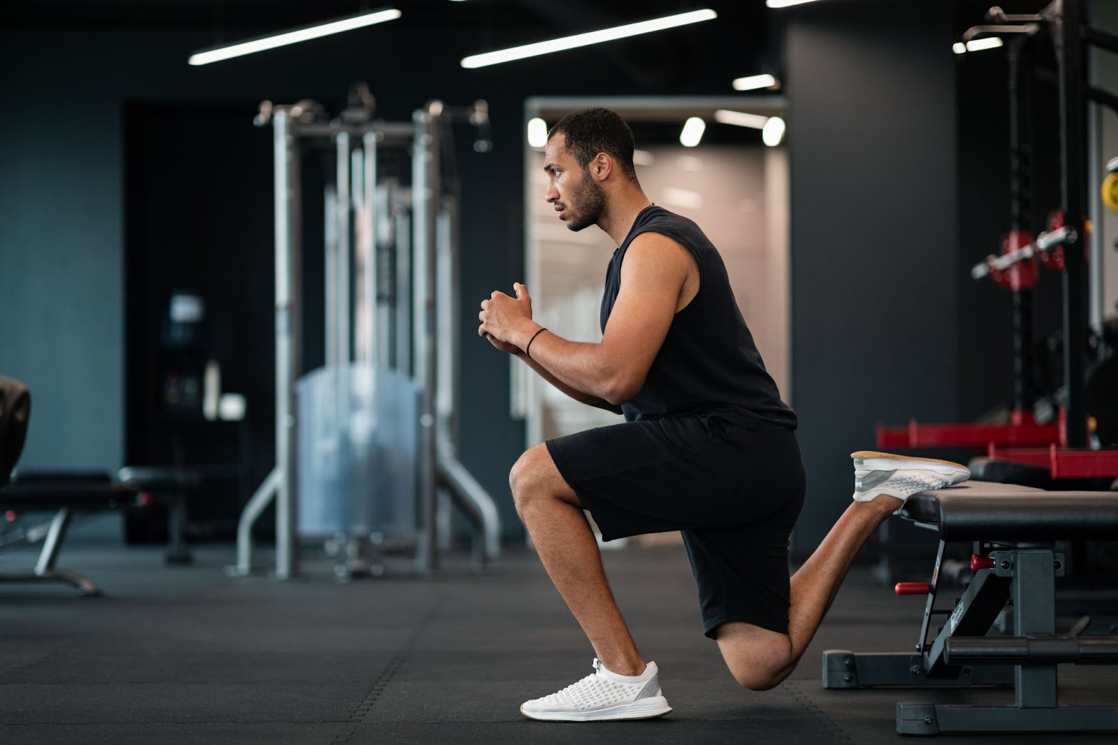 Man in black tank top doing a Bulgarian split squat in a gym