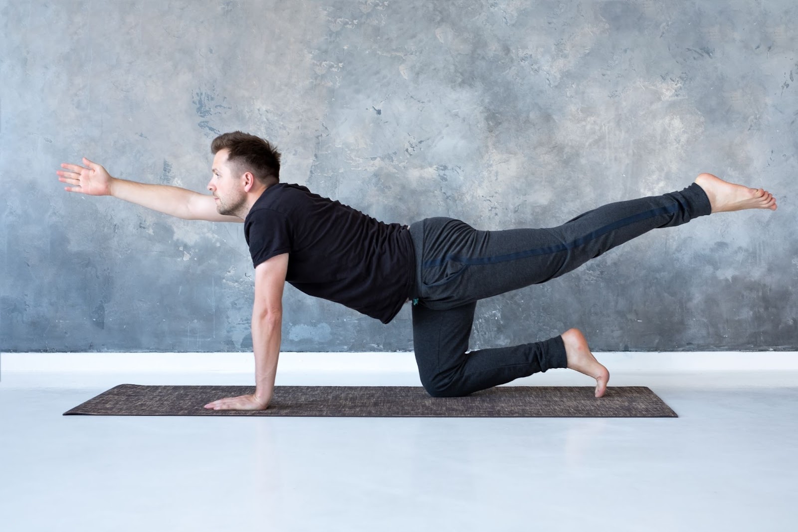 man dressed in black doing a Bird Dog Pilates exercise movement