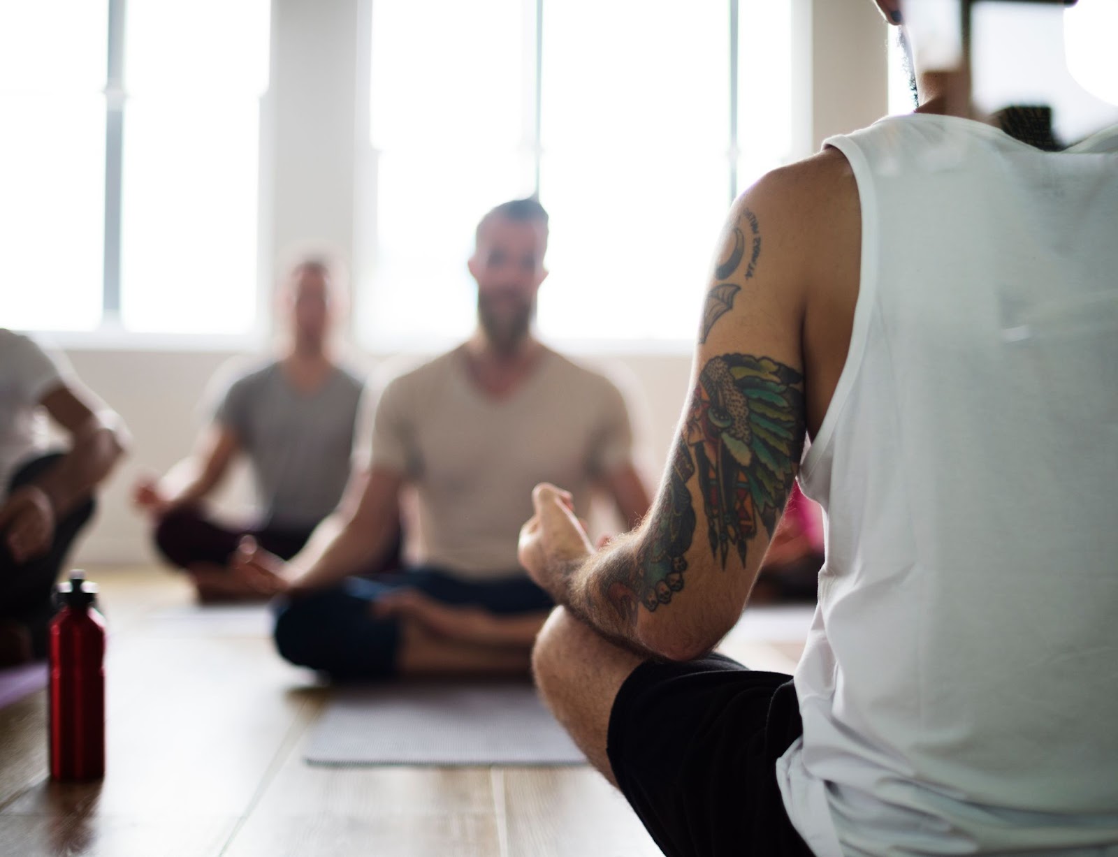 A tattooed man teaches a male yoga class