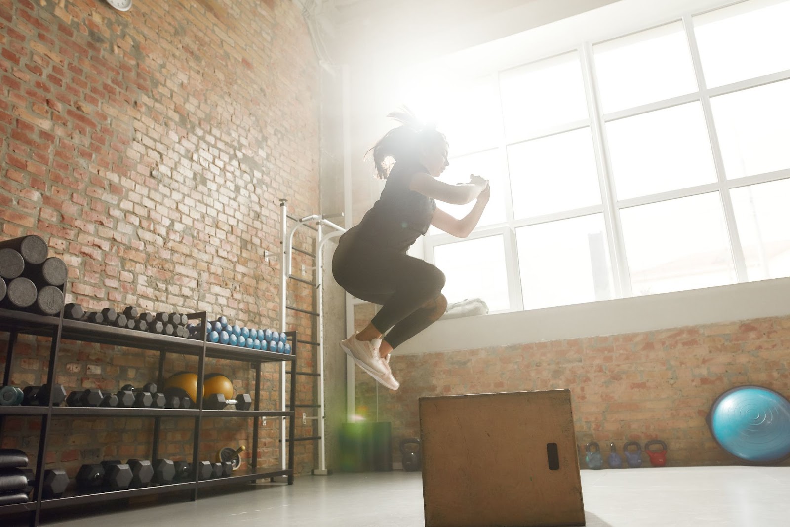Woman performing a box jump on a plyometric box in a brick gym
