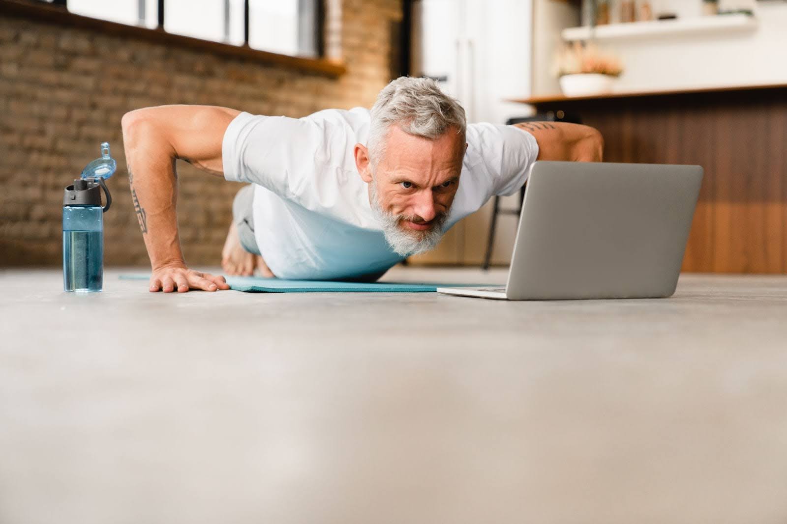Fit elderly man practicing yoga at home in front of a laptop
