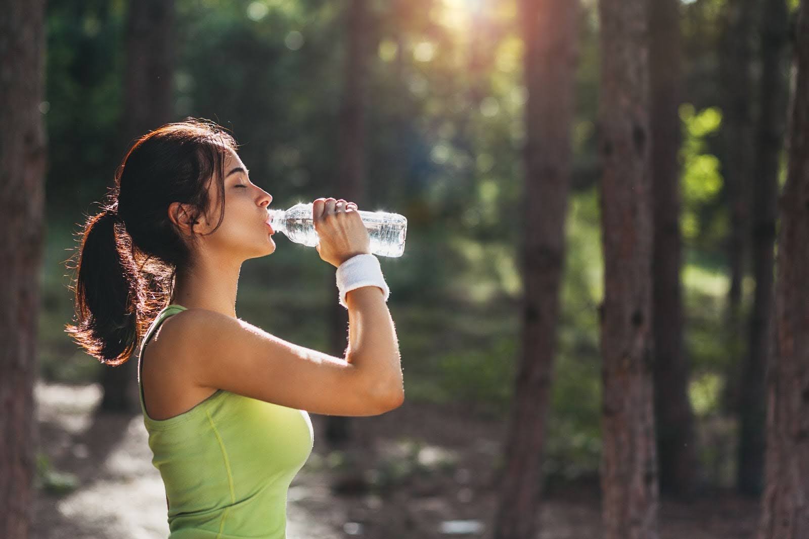 Fit woman drinking water outside in a forest