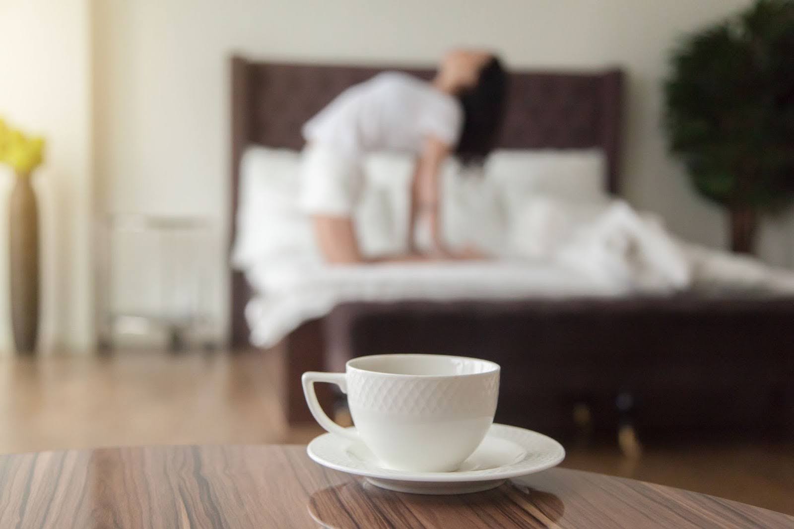 Fit woman stretching in her bed, about to drink a cup of coffee before her workout