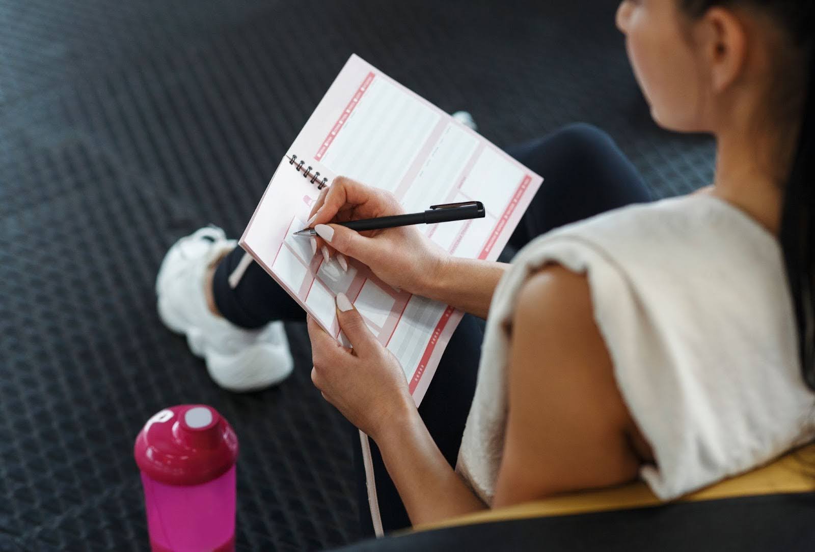 Fit woman writing down in a notebook her fitness schedule