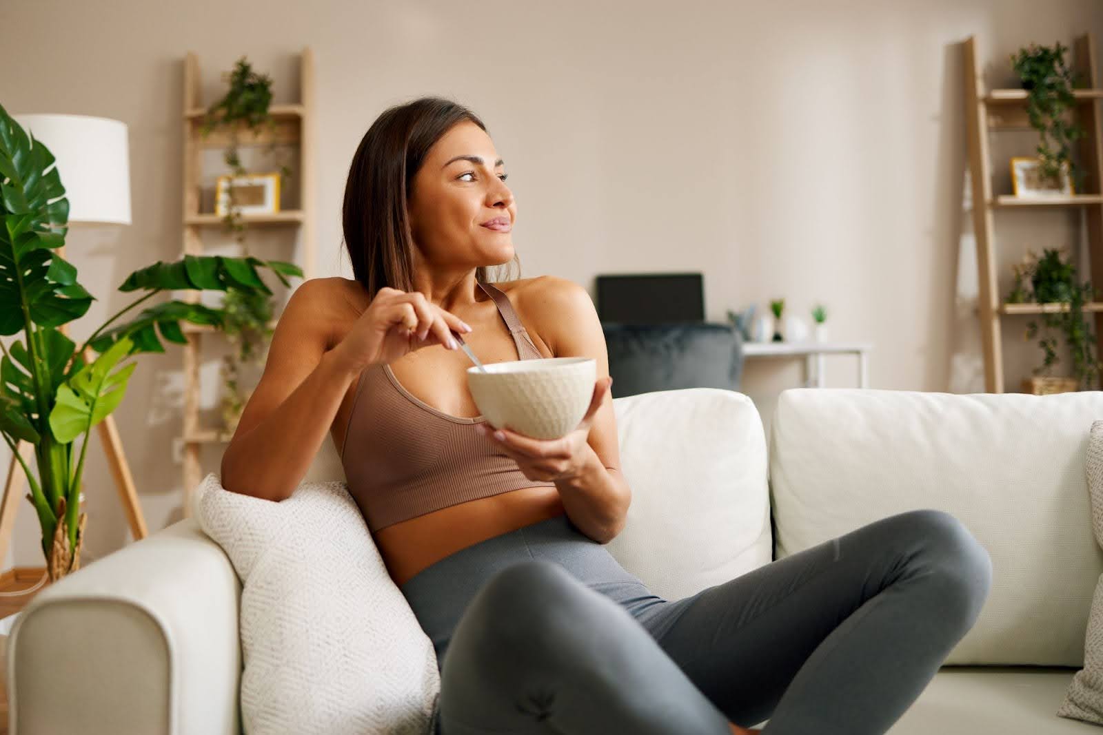 Fit, beautiful woman sitting on a couch, eating a small and healthy meal