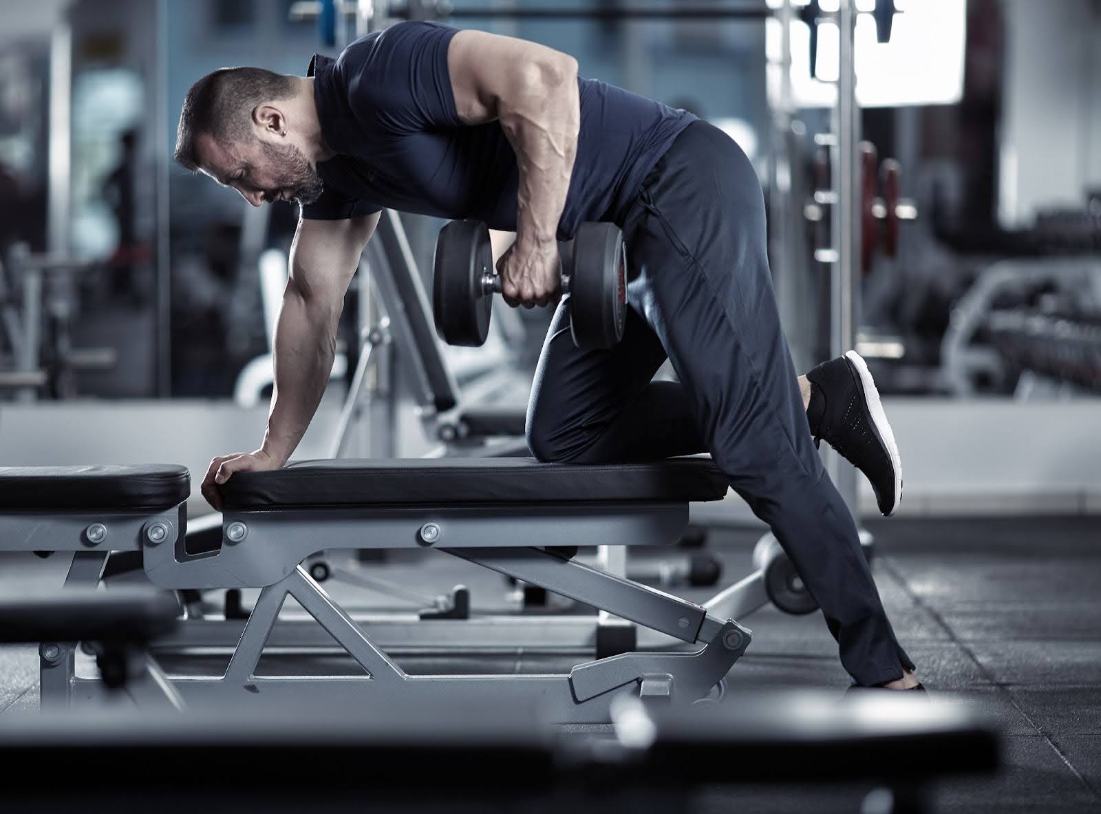 Image of strong man performing a single arm dumbbell row in a gym