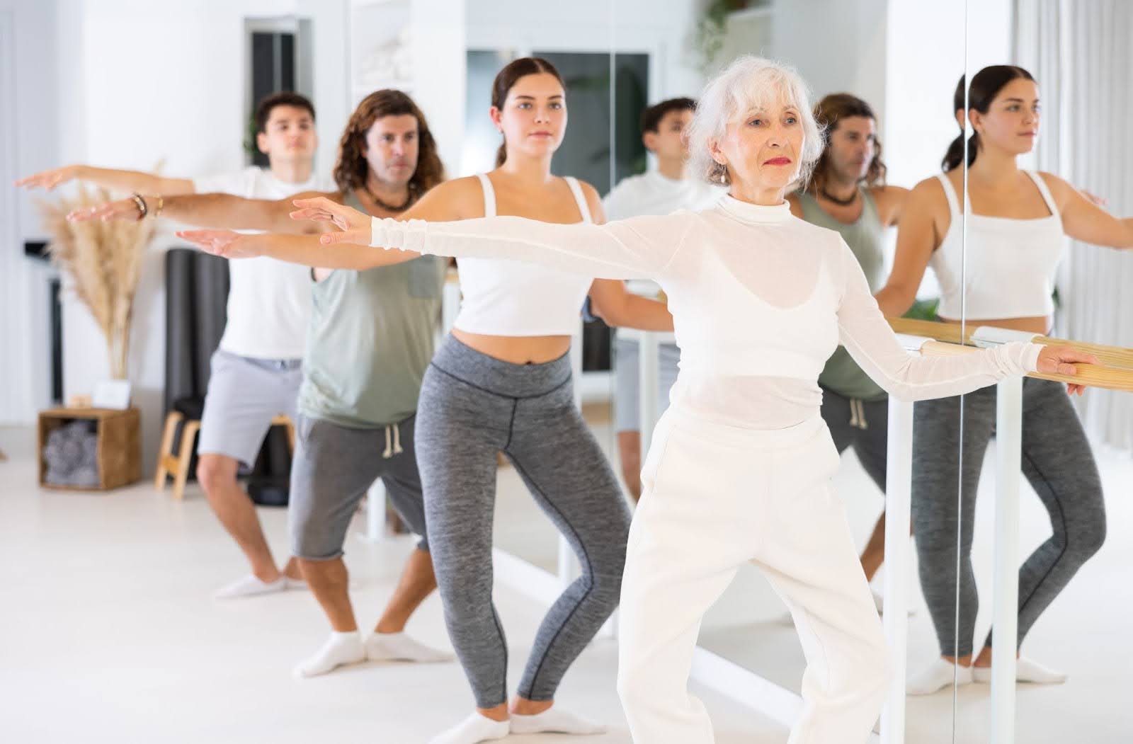 Multi-gendered group of people performing plie movements in a Barre class