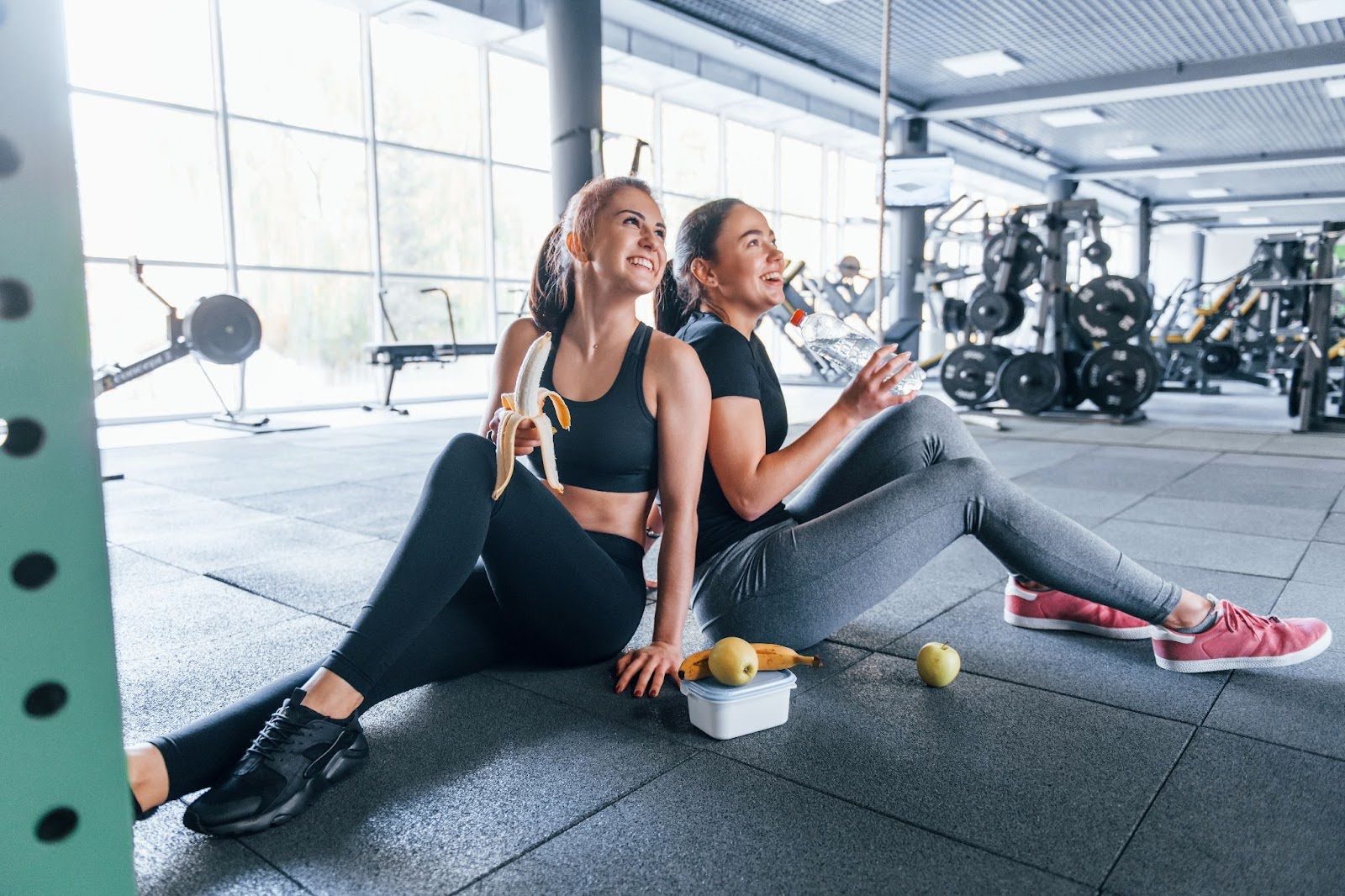 Two fit young women sitting in the gym, eating breakfast