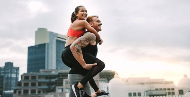 Very fit couple, with woman riding on man’s back, in an urban environment
