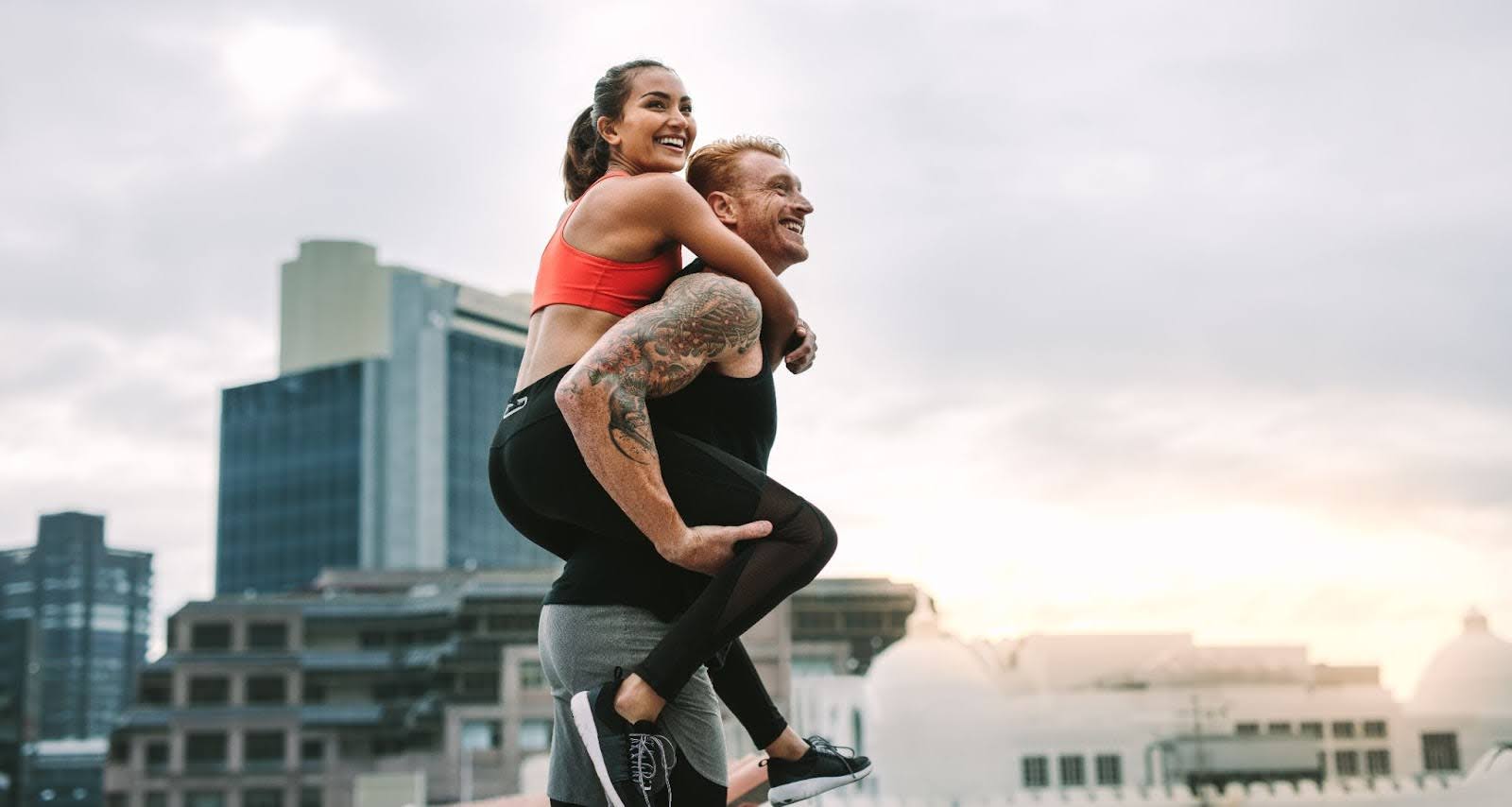 Very fit couple, with woman riding on man’s back, in an urban environment
