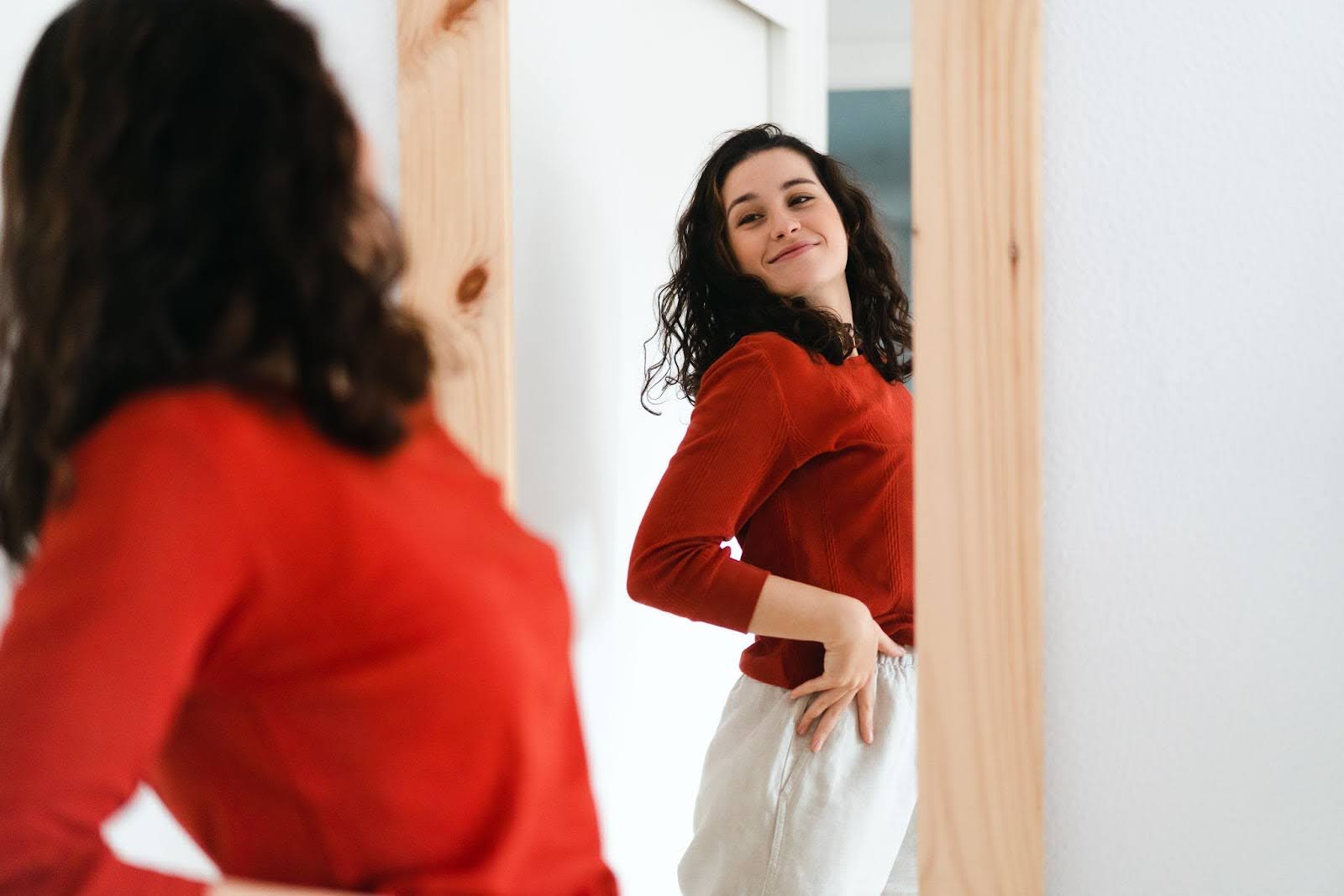 Woman smiling looking at herself in the mirror in a red shirt and white pants