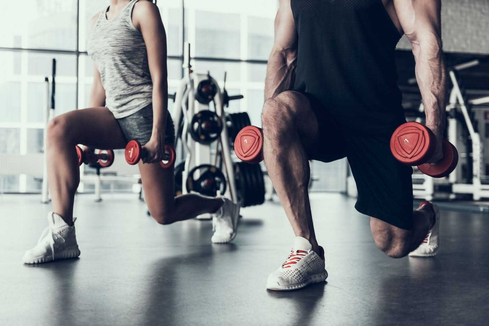 A strong man and woman doing lunges in a gym