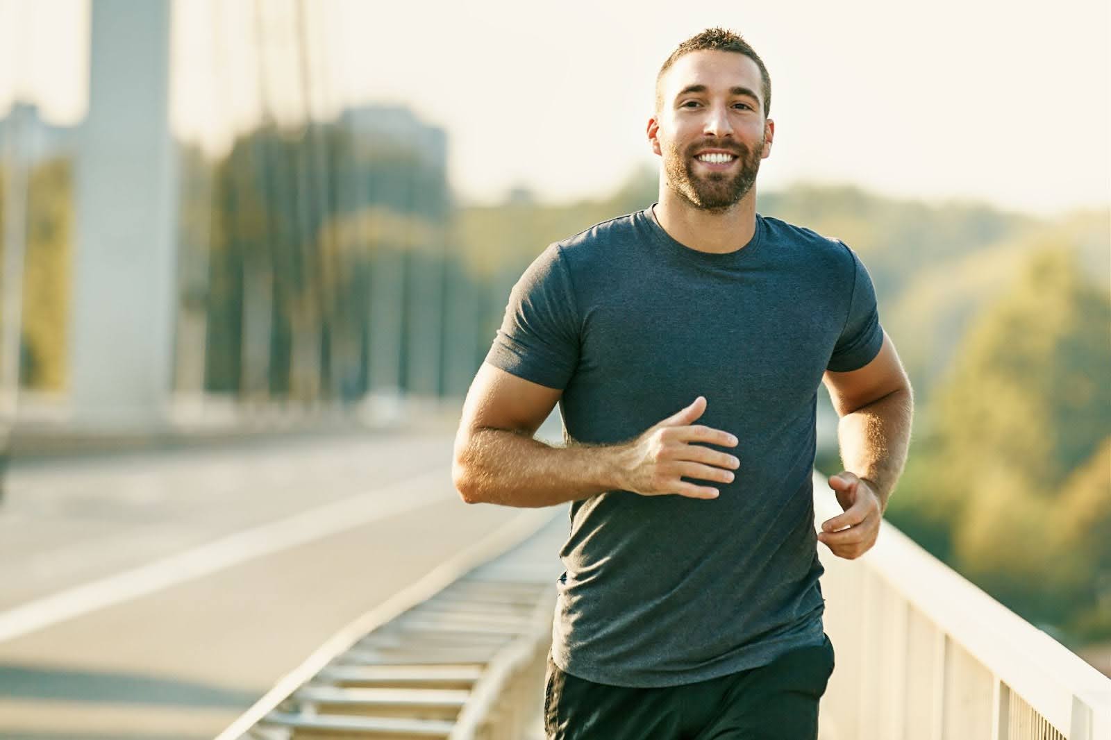 Fit man in a blue shirt running outside on a bridge