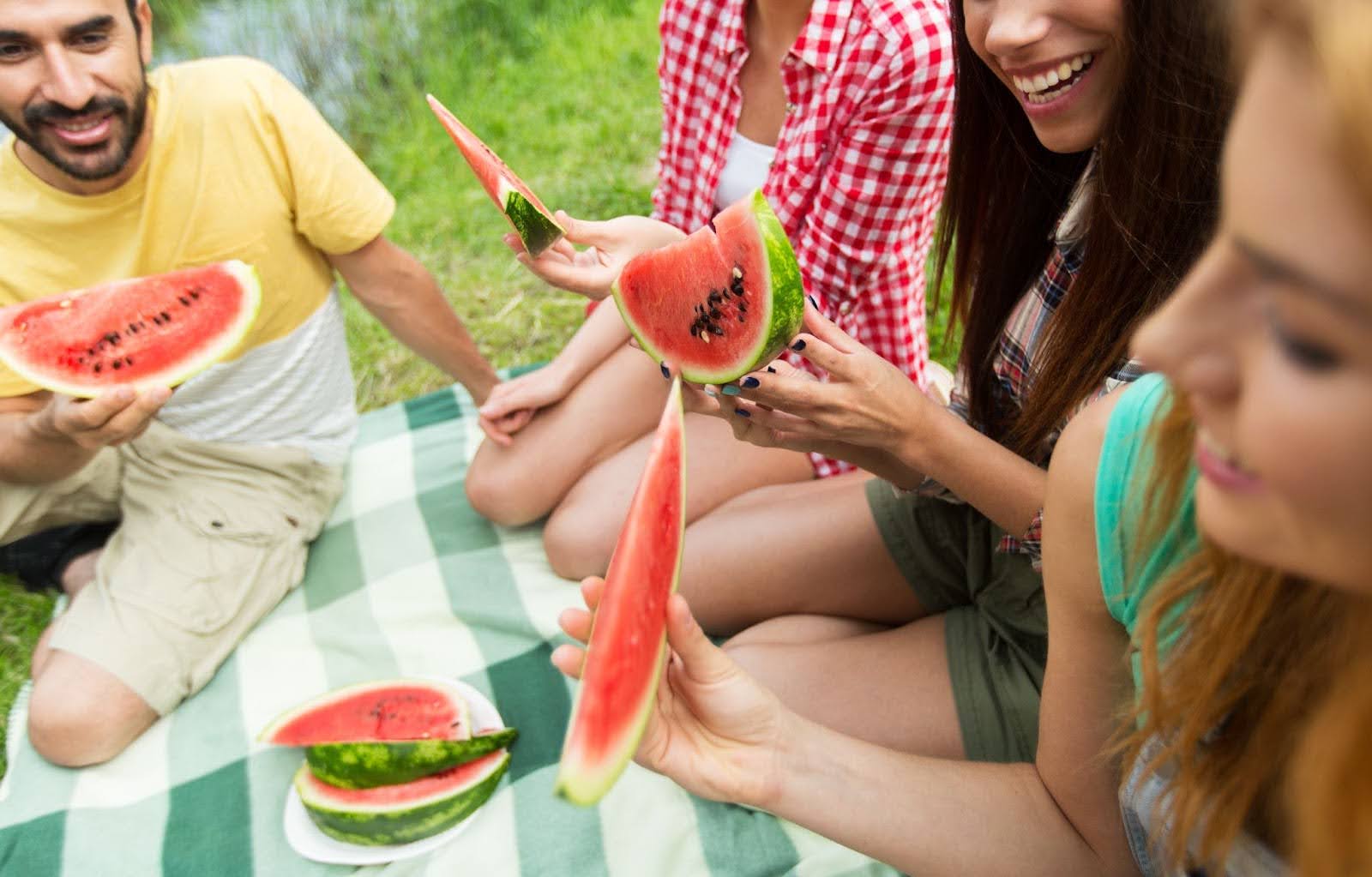 A group of smiling people eating watermelon in a park