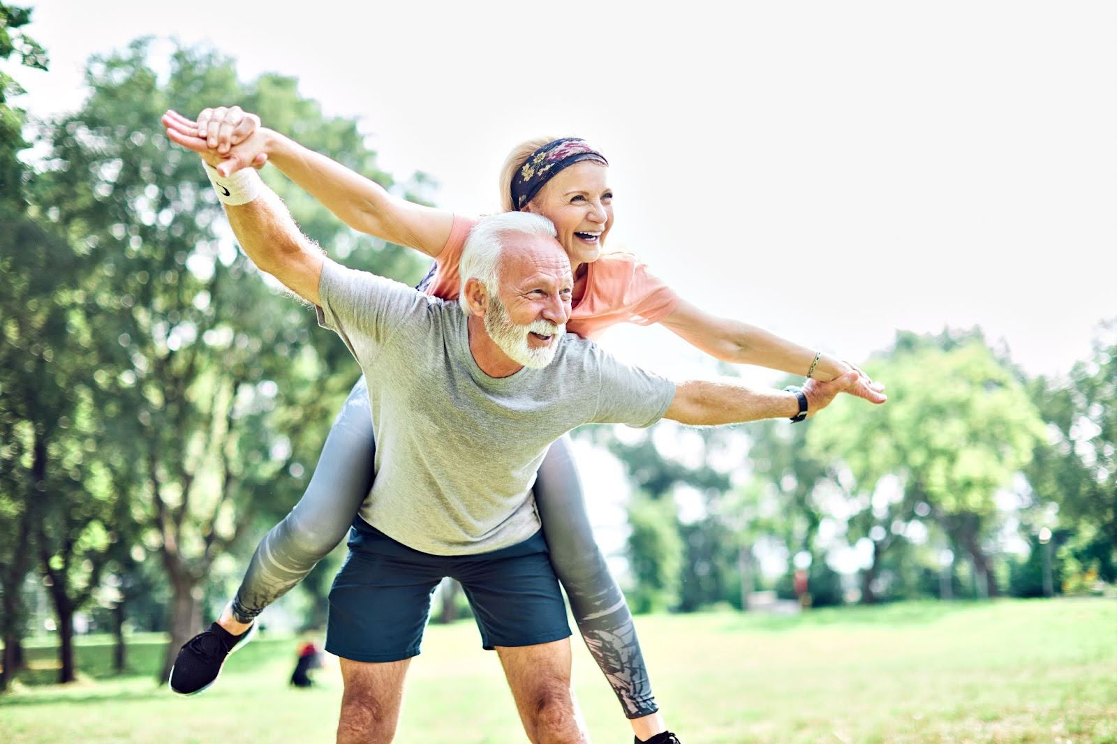 Couple of senior citizens, with an older woman smiling and lying on the older man’s back